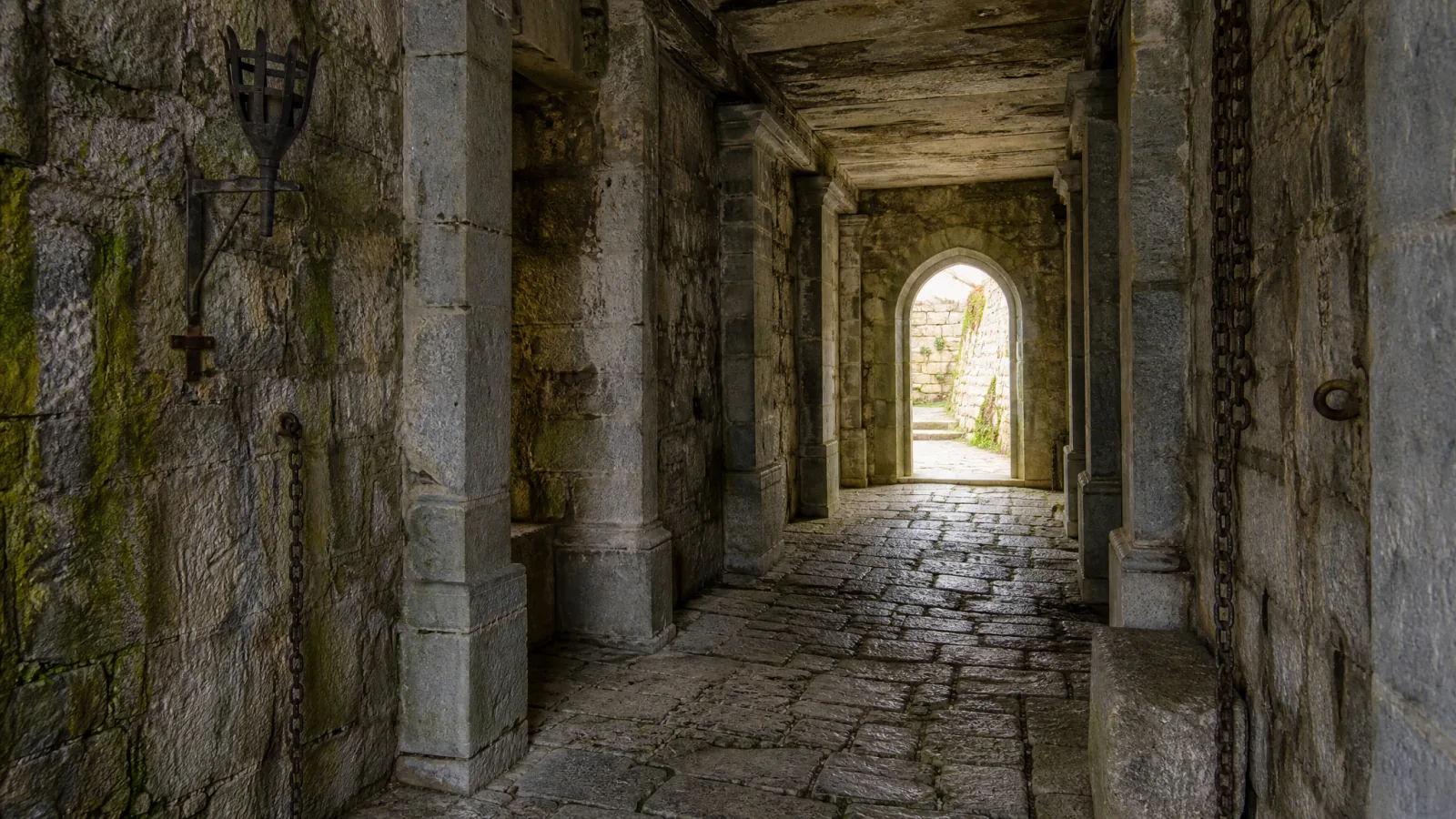 A stone corridor reference photo with an arched doorway, a hanging lantern and a carved wall sconce
